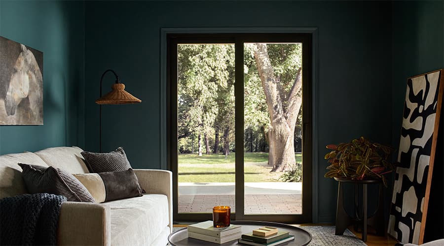 A black sliding patio door brings light into a dark green living room.