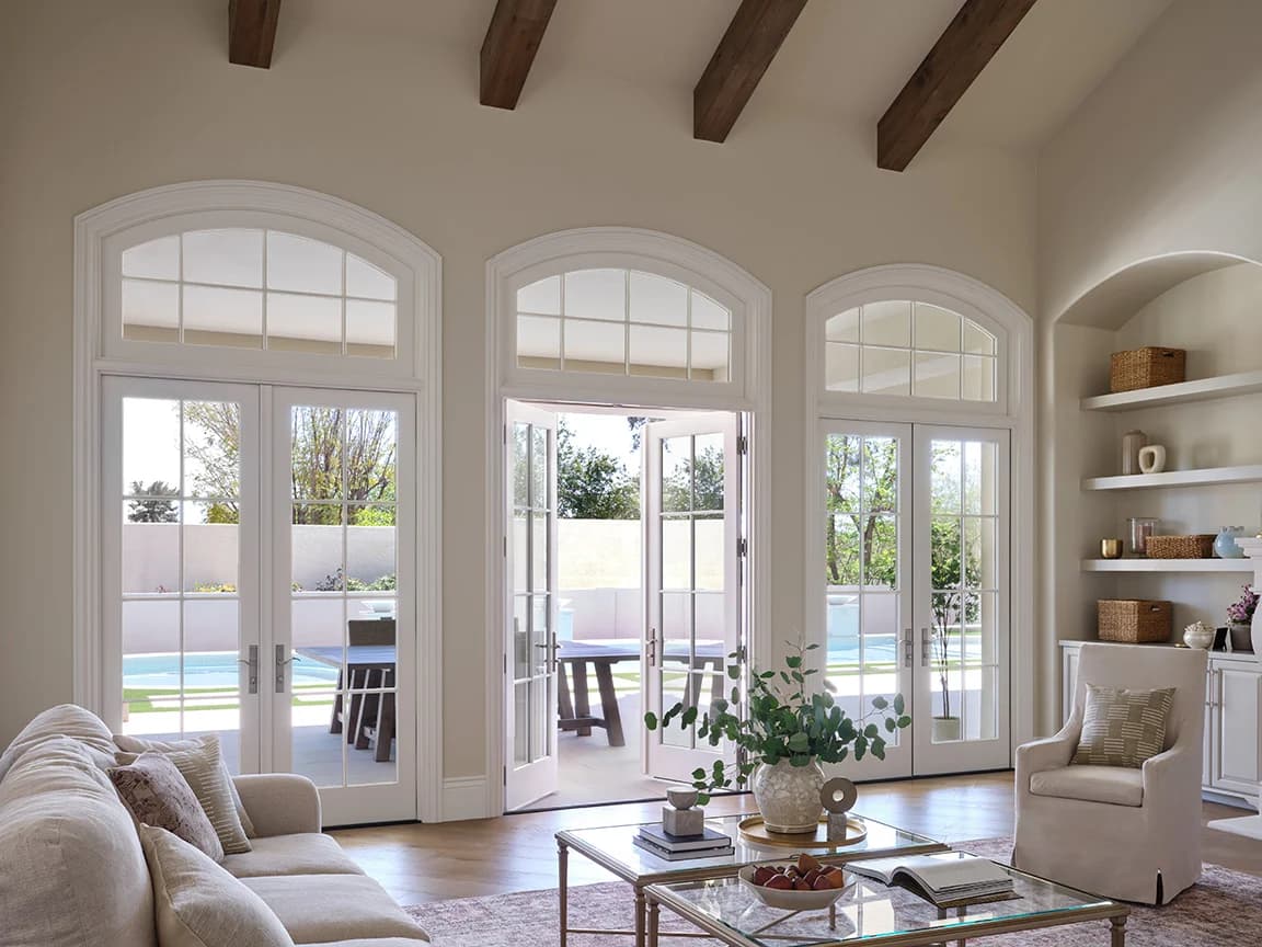Bright living room with white hinged-doors and large arched windows opening to a patio.