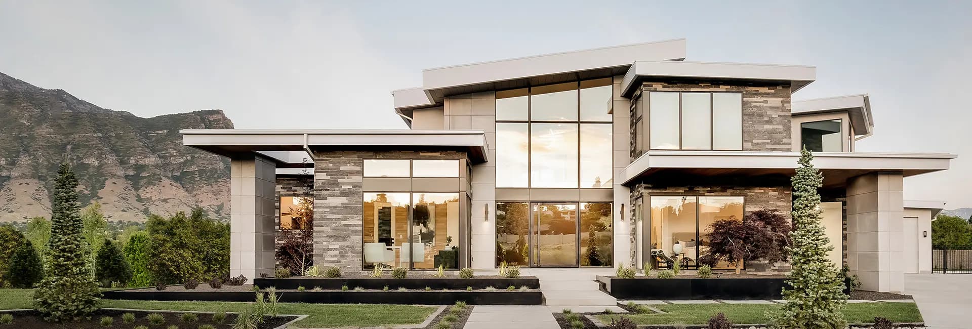 Contemporary luxury home with floor-to-ceiling windows, mixed stone facade, landscaped front yard and mountain backdrop