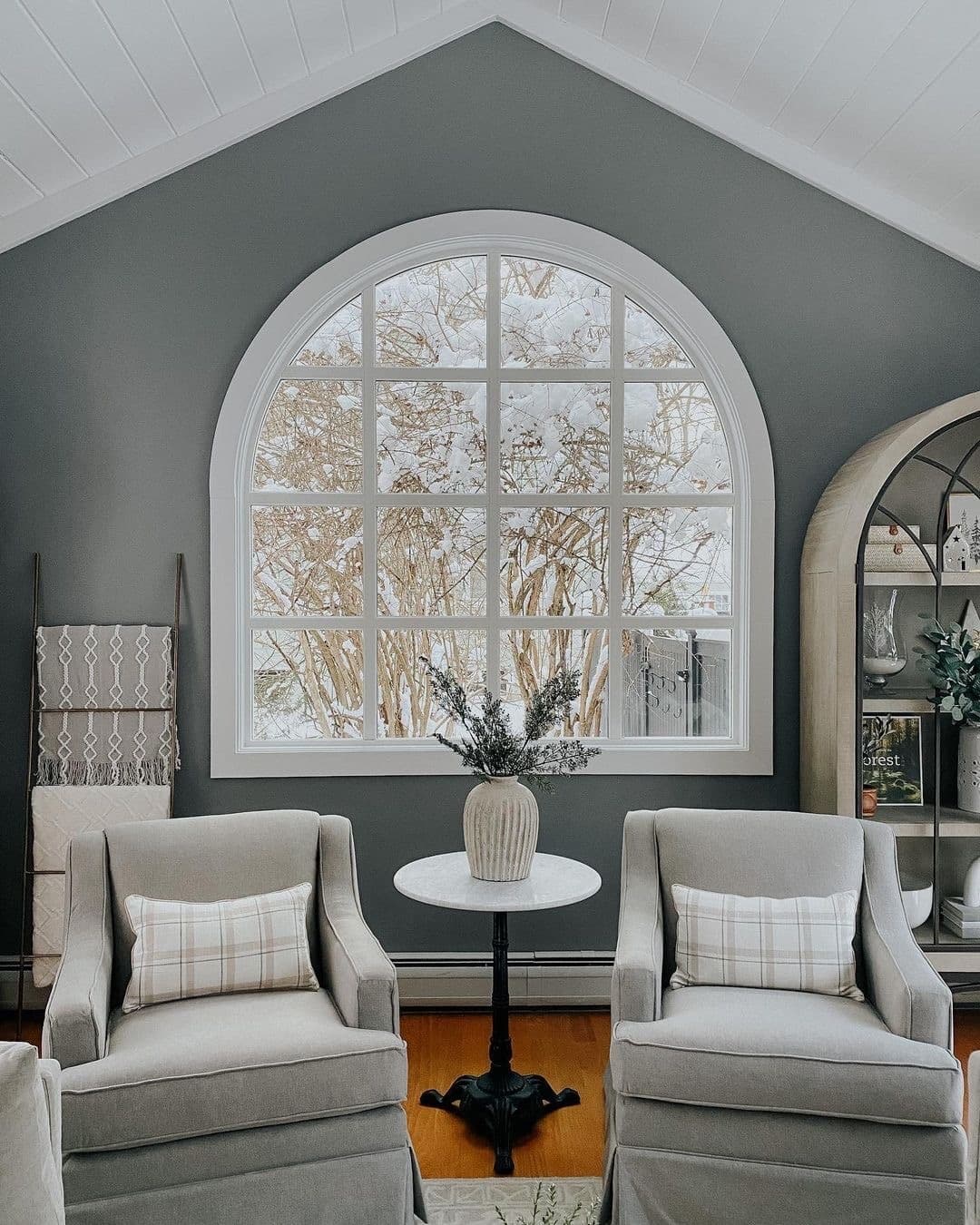 A large white arch window with grilles lies behind two gray chairs in a seating area.