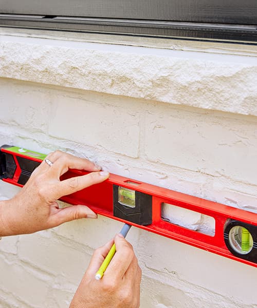 Using a level to ensure the marking on an exterior home wall doesn't angle up or down.