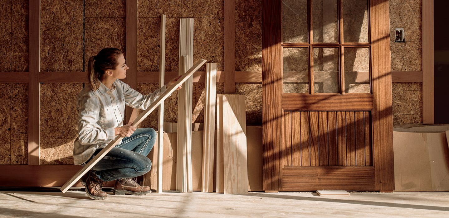 a female construction work is examining a piece of trim by a wood entry door