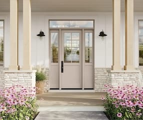 Black front door with glass panes on a white farmhouse porch, flanked by matching sconces, iron railings, and potted purple flowers.