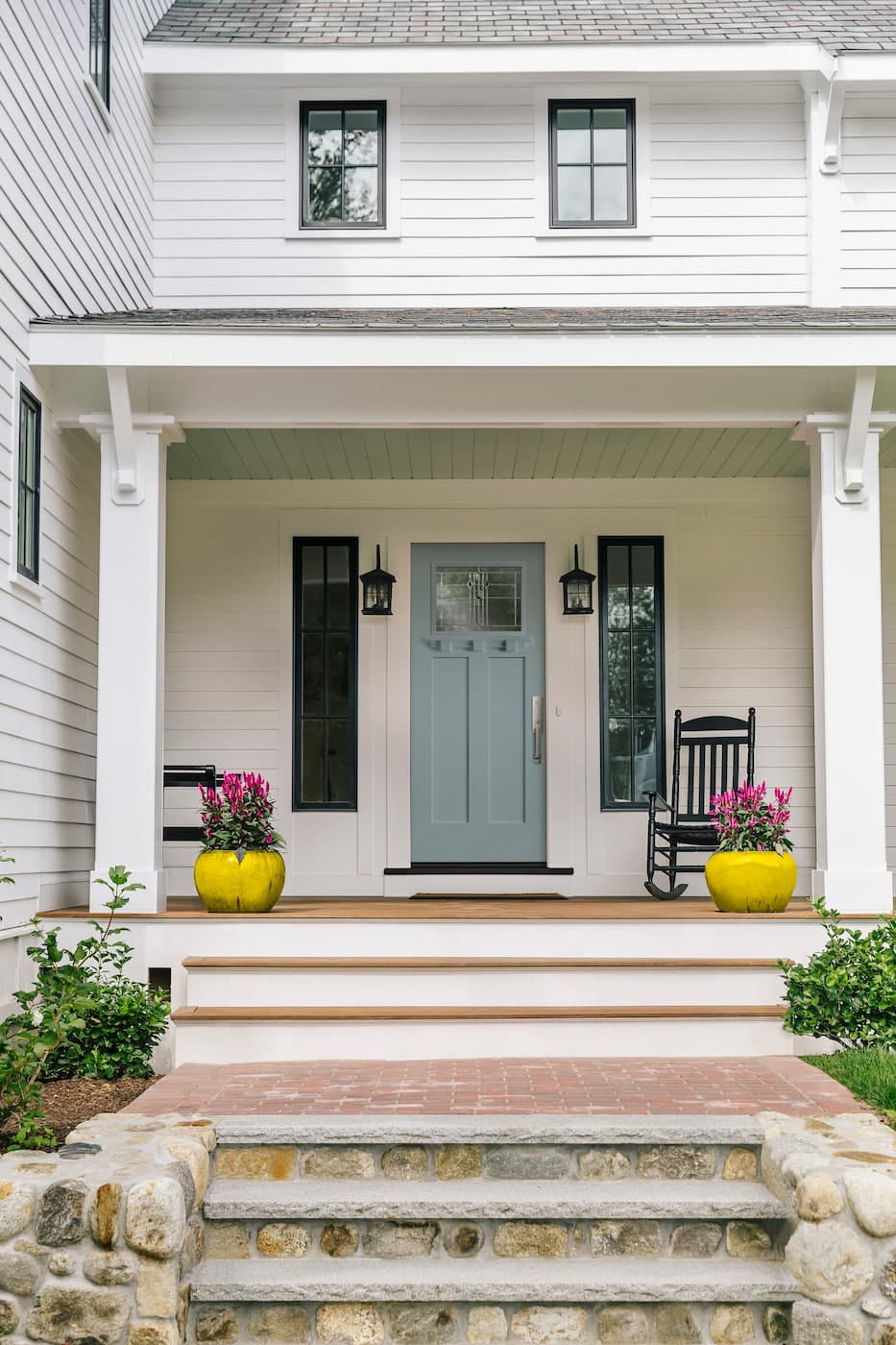 Blue Craftsman Front Door Draws Eyes To Welcoming Entryway Blue craftsman front door with decorative glass and modern hardware surrounded by black windows on white house