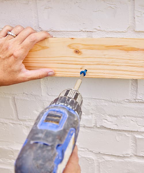 Using a screwdriver to attach a board to a home exterior that will be used to hang a window box.