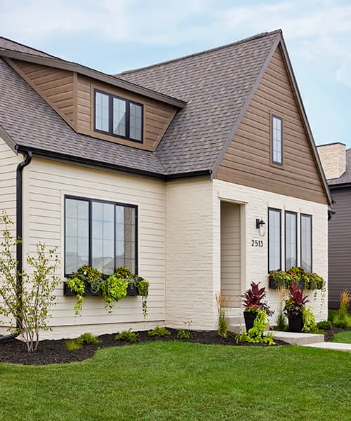 A home exterior that has window boxes filled with several varieties of greenery as well as front potted plants aside the entrance.