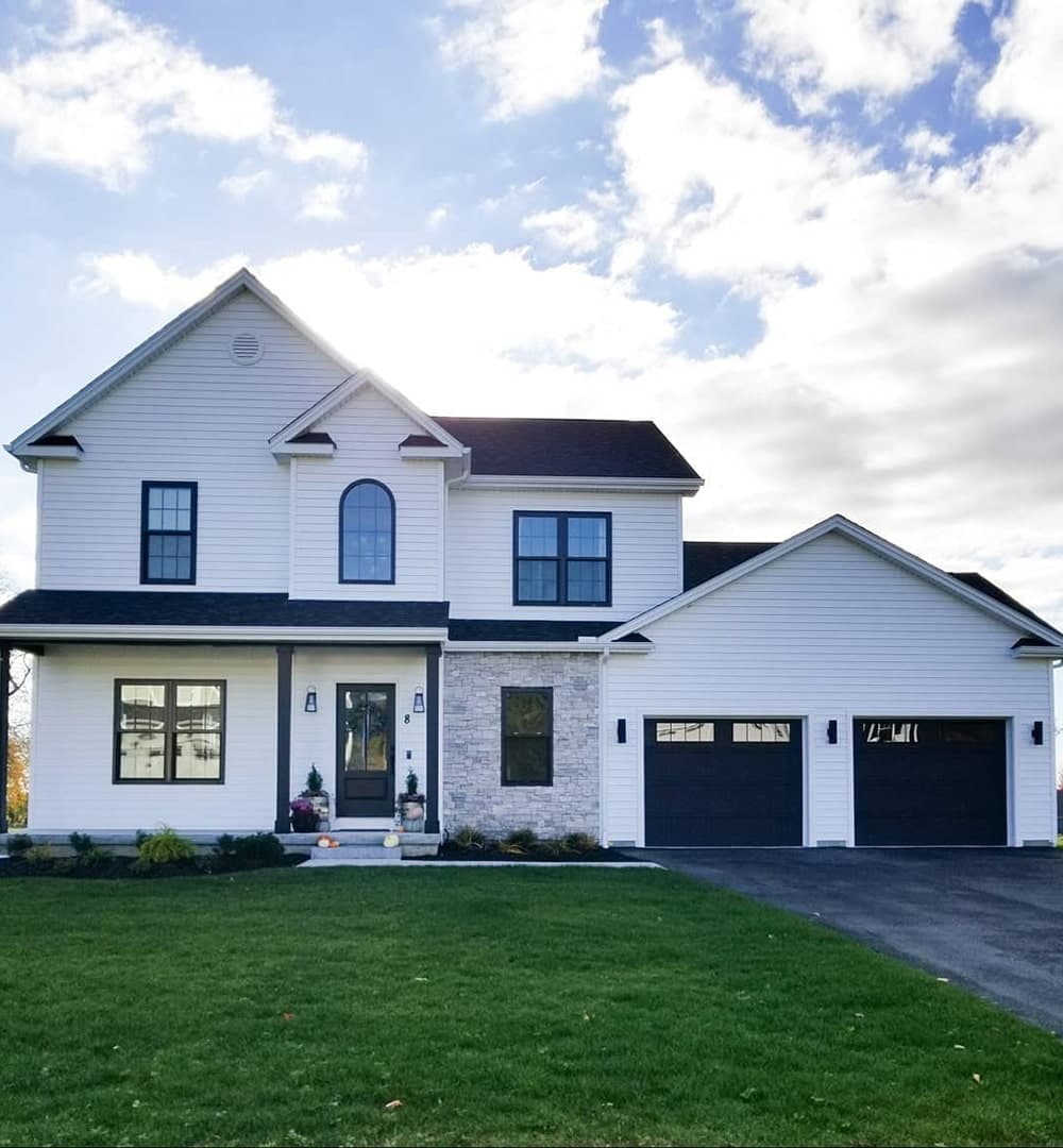 A white farmhouse exterior features black double-hung and picture windows, including a custom arch window over the front door.