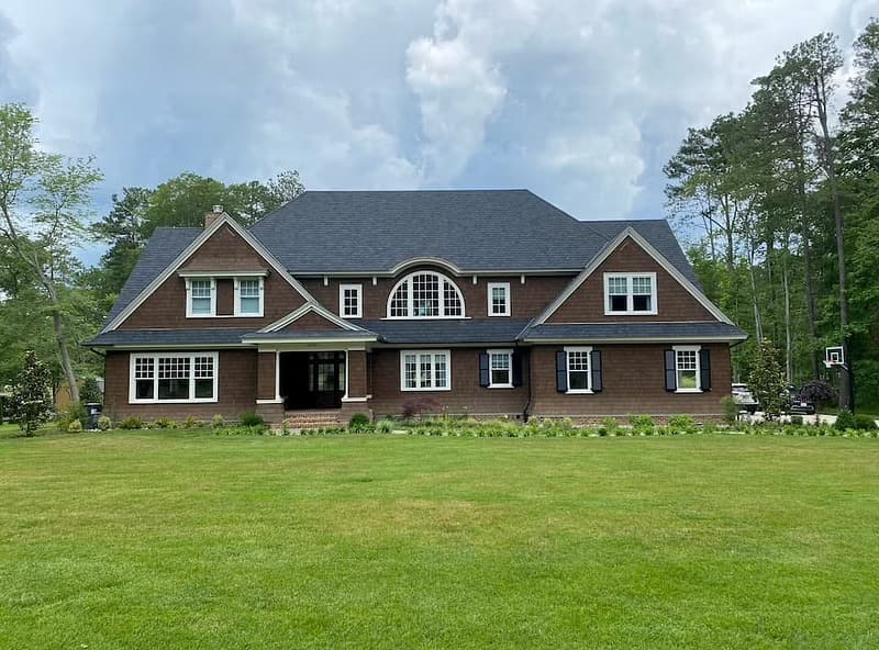 The exterior of a brown craftsman house has white windows, including an arch window in the center.