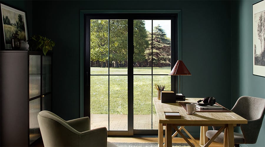 A black sliding patio door leads to the outside from a dark home office.