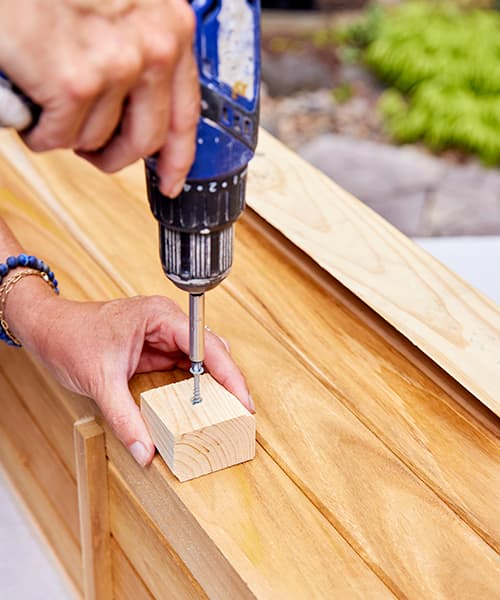 Using a drill to screw a wood spacer to the wood window box
