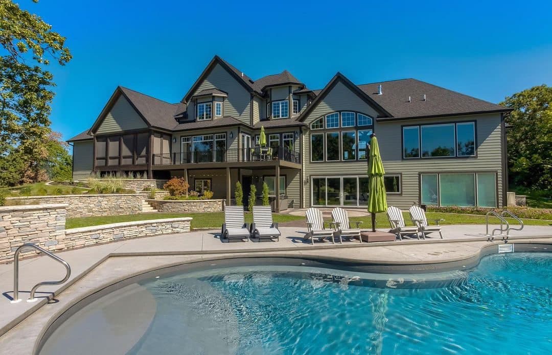 The exterior of a traditional brown house with sliding patio doors and picture windows overlooks a pool in the backyard.