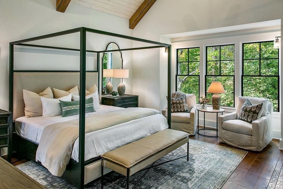 A neutral-color bedroom features black single-hung windows along with a black metal bed canopy.
