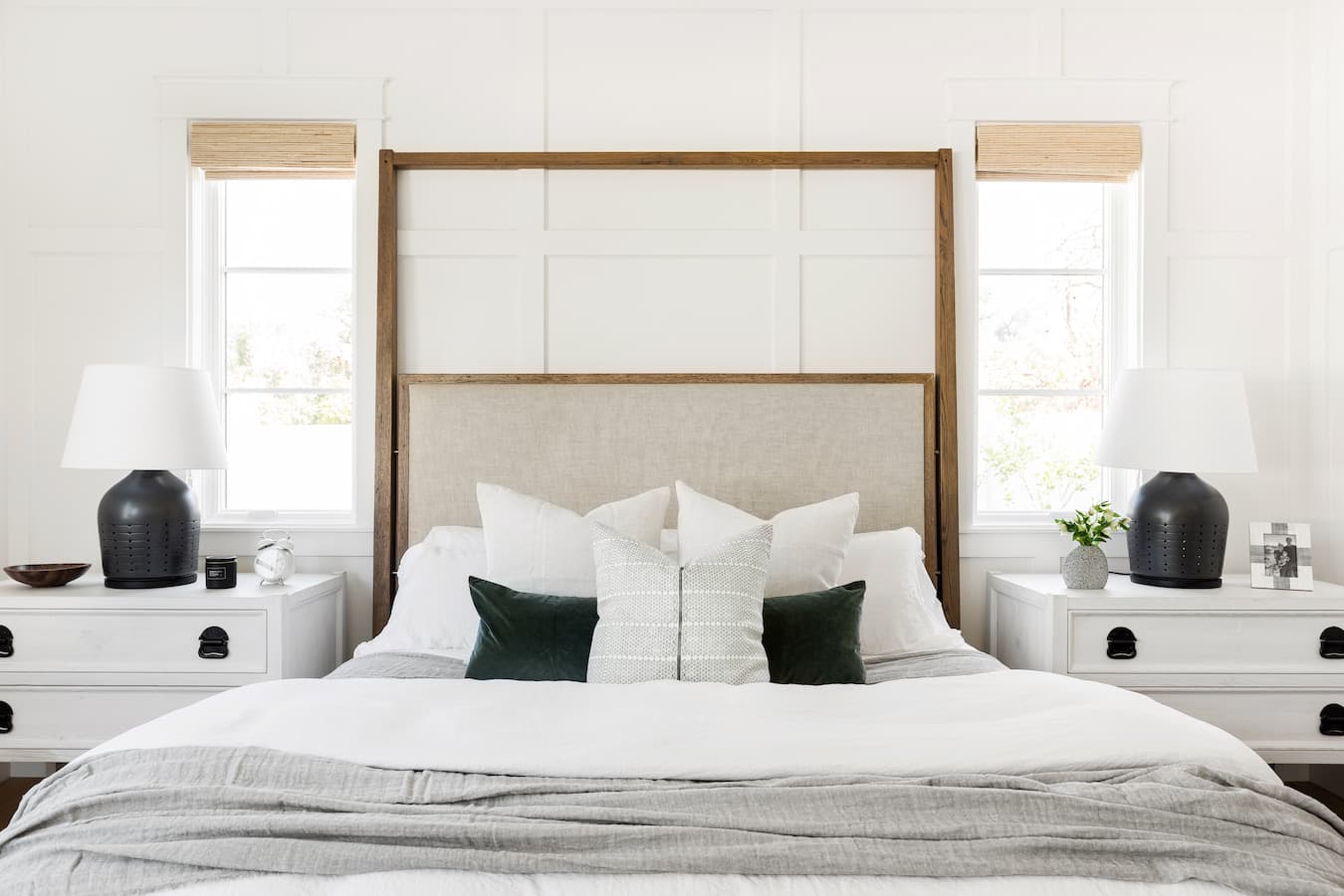 A bedroom has a wood headboard, black and white bedding and white windows above each nightstand.