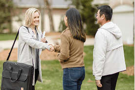 A saleswoman wearing a long gray coat is shaking hands with a woman while a man stands nearby.