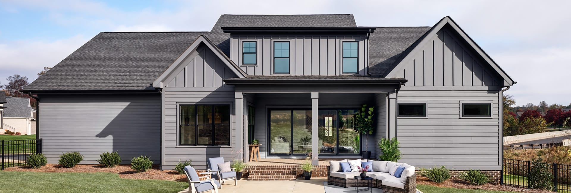Modern gray farmhouse exterior with covered front porch, brick steps, patio seating and landscaped lawn