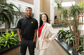A young man and woman are standing in a large courtyard smiling at the camera.