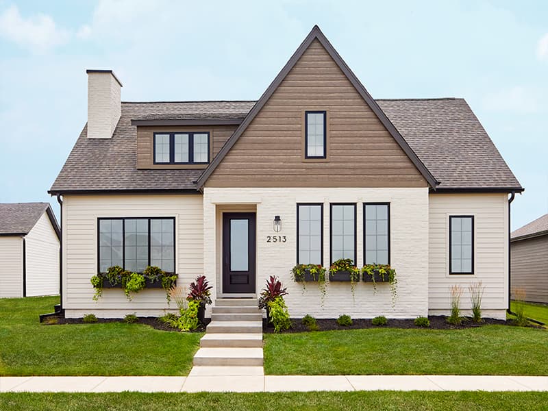 window boxes with a wide variety of flowers and green plants sit below several front windows on a white brick home